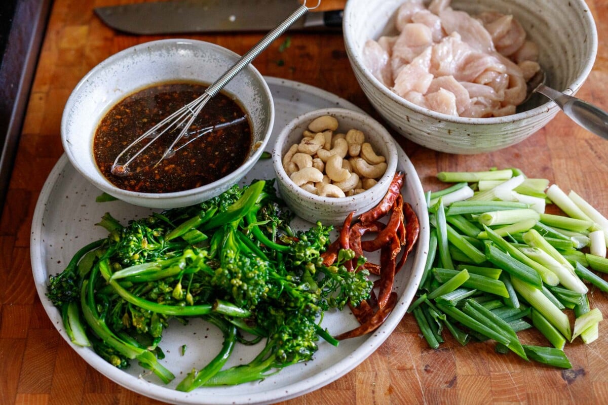 szechuan chicken stir fry ingredients prepped by stove and ready for cooking - cashews, dried chilies, broccolini, stir fry sauce, chicken