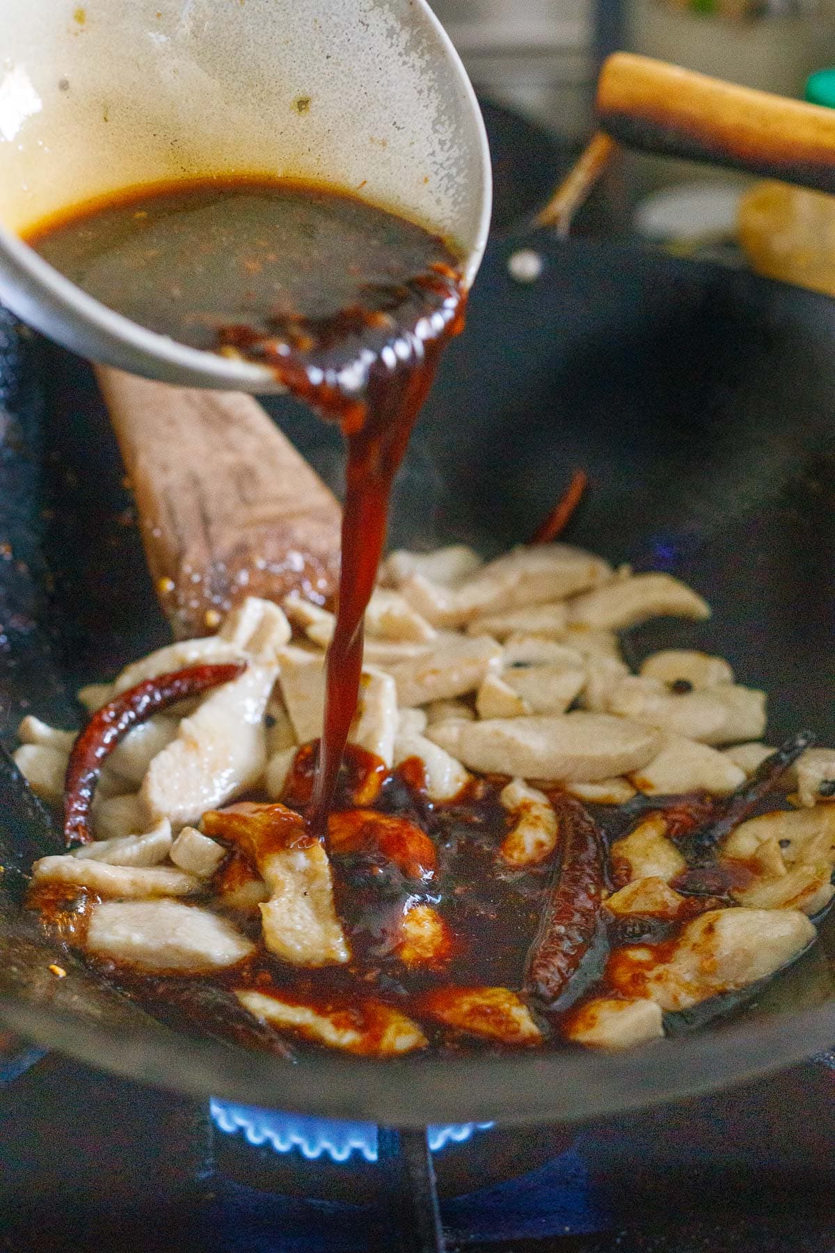 pouring szechuan sauce over the chicken and dried chilies in wok 