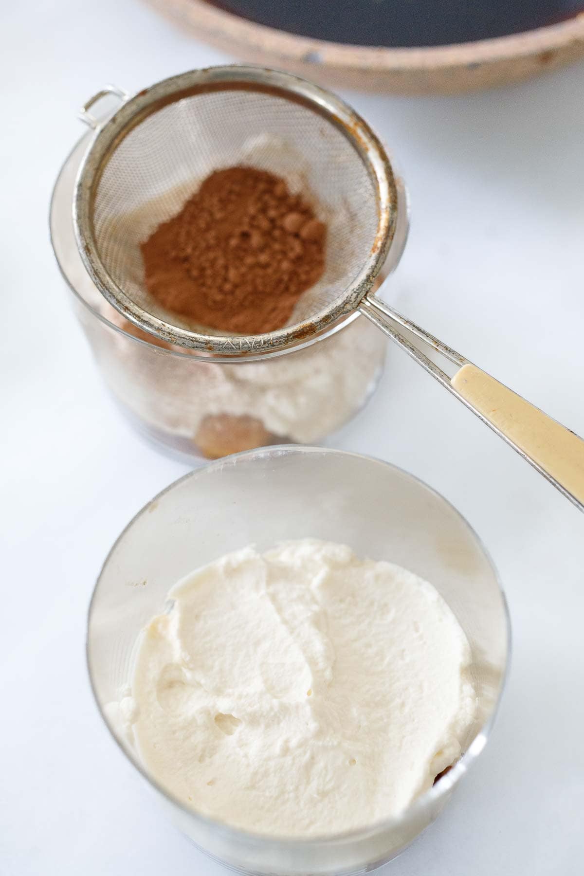 making tiramisu in glasses - dusting cocoa powder over top of whipped mascarpone mixture
