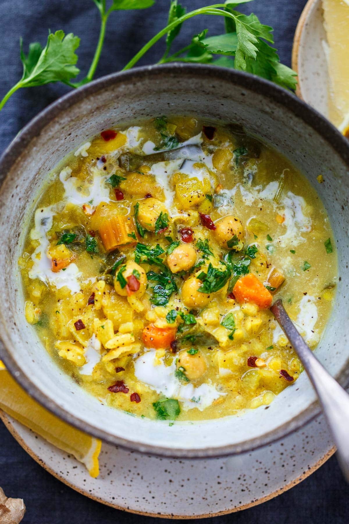 coconut chickpea soup in bowl with spoon, full of chickpeas, carrots, rice, red pepper flakes, coconut milk, parsley.