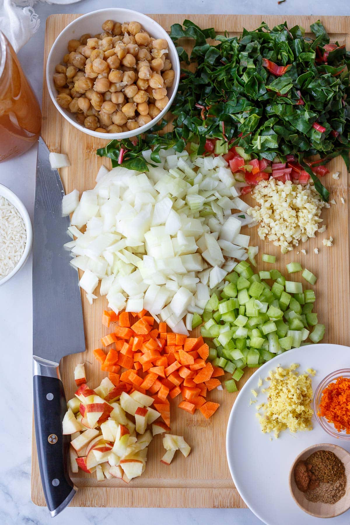 wood cutting board with ingredients for chickpea soup diced - chard, onion, garlic, celery, carrots, apple.