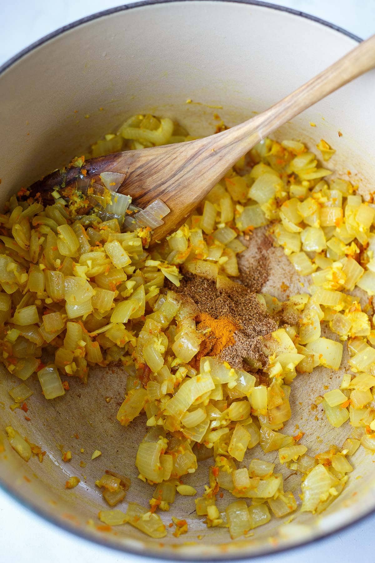 diced onion and grated ginger and turmeric with spices stirred in soup pot with wooden spoon.