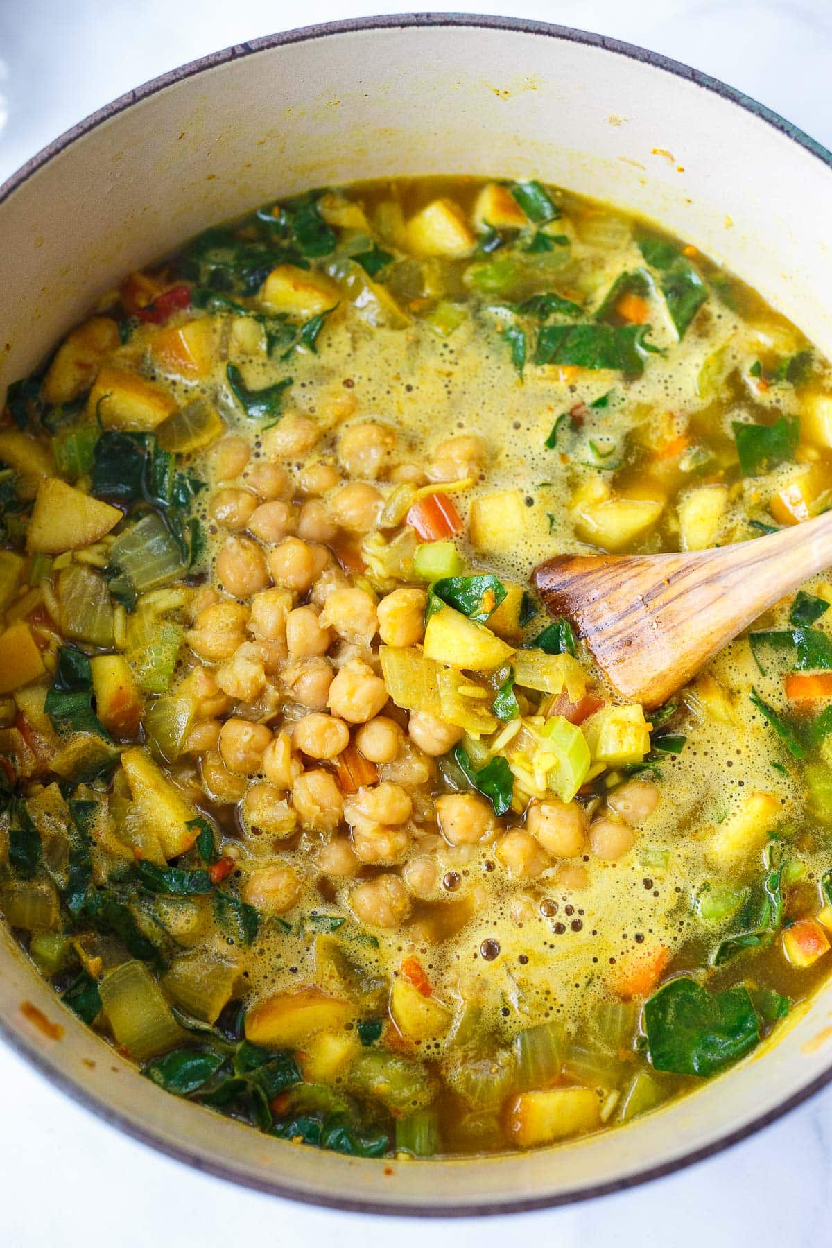 chickpea soup cooking in pot with diced vegetables and dark, leafy greens.