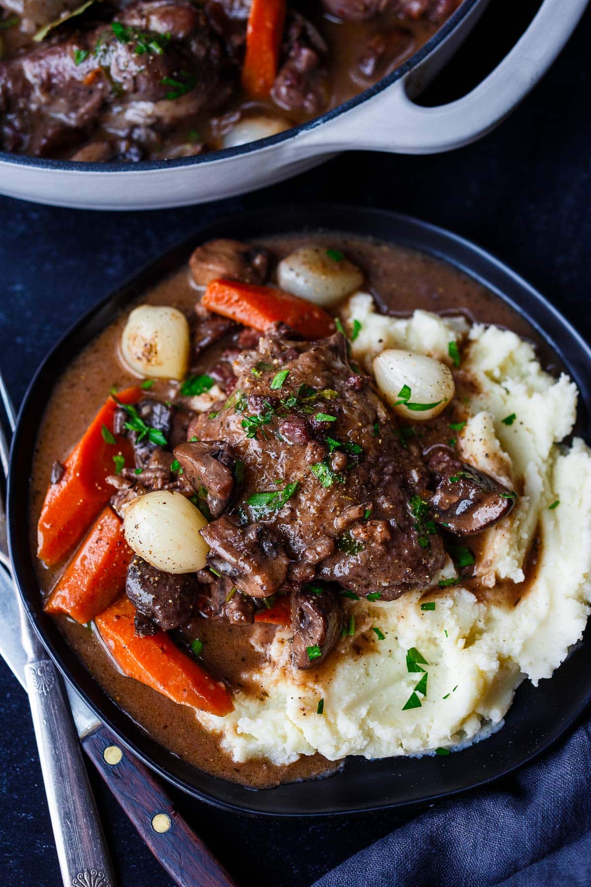 coq au vin served on plate over mashed potatoes, garnished with fresh parsley.