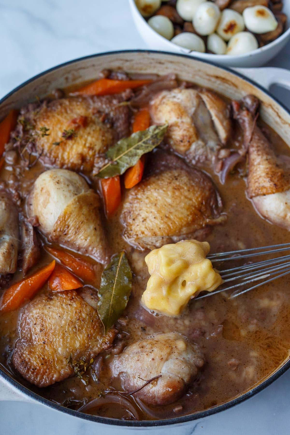 coq au vin in large dutch oven with flour and butter mixture being whisked in.