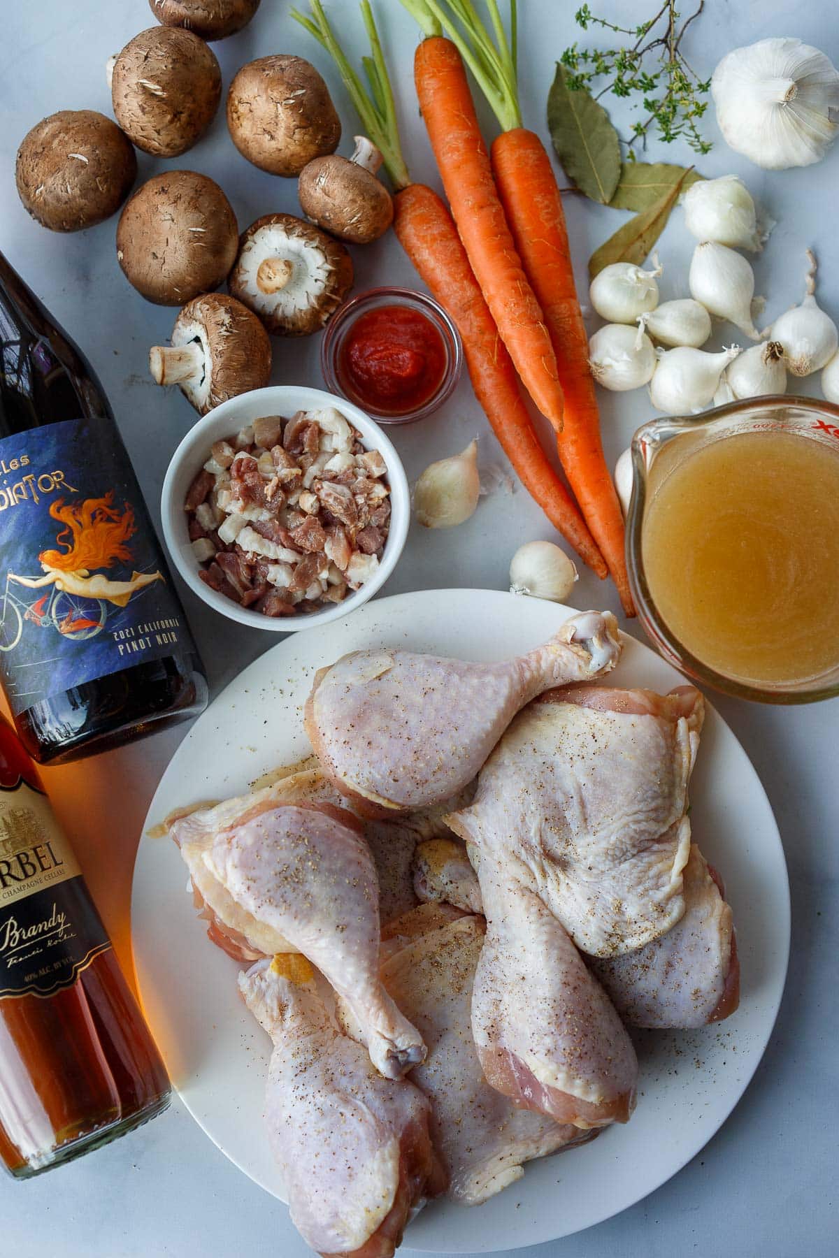 ingredients for coq au vin- garlic, thyme, bay leaves, pearl onions, broth, carrots, tomato paste, mushrooms, pancetta, pinot noir, brandy, chicken thighs and drumsticks.