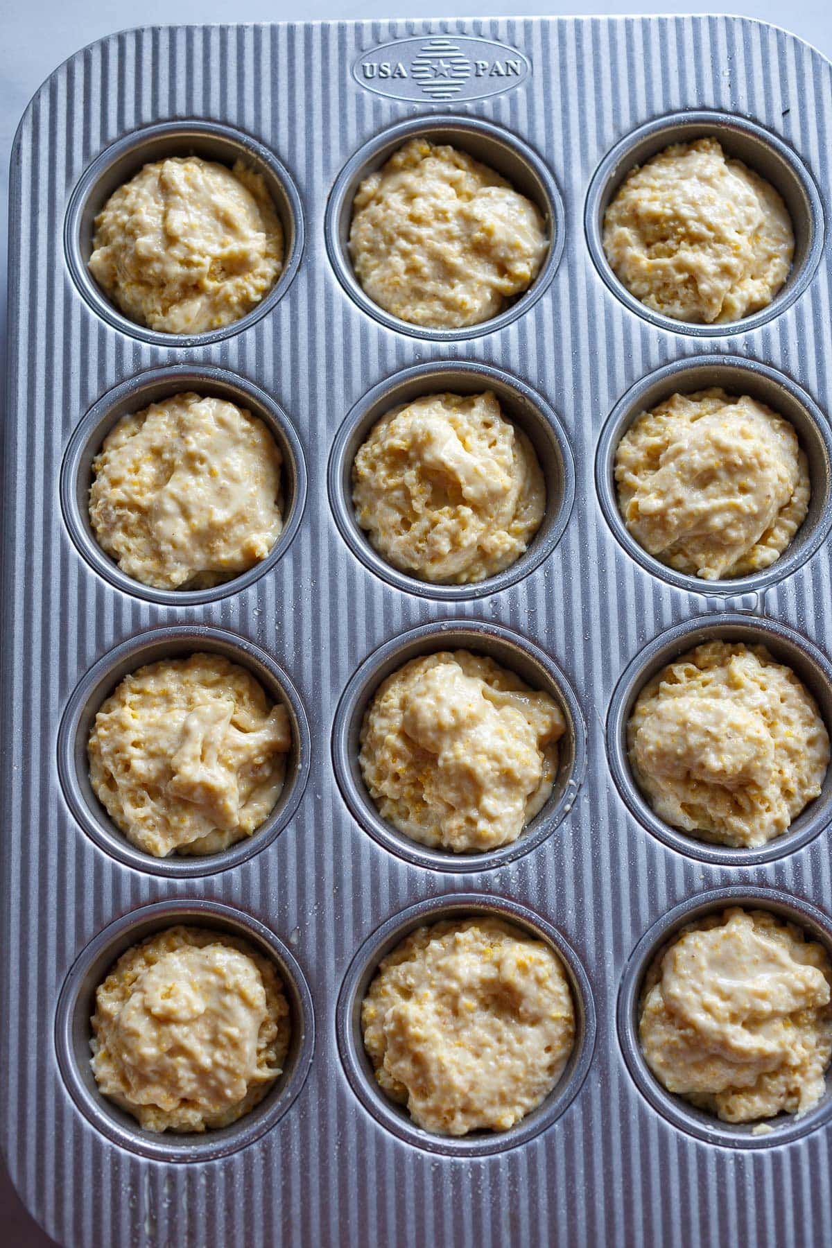 vegan cornbread muffin batter in muffin tins with 1/4 inch of space left at the top of each.