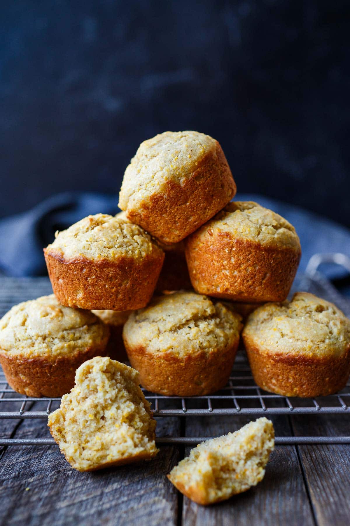 vegan cornbread muffins stacked on top of a cooling rack with a split muffin in front.