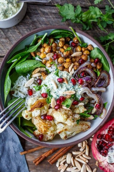 You'll love these roasted Cauliflower Chickpea Bowls! Spiced cauliflower and chickpeas served over Moroccan rice with spinach, almonds, and pomegranate seeds. A tasty wholesome dinner bursting with flavor! Vegan-adaptable.