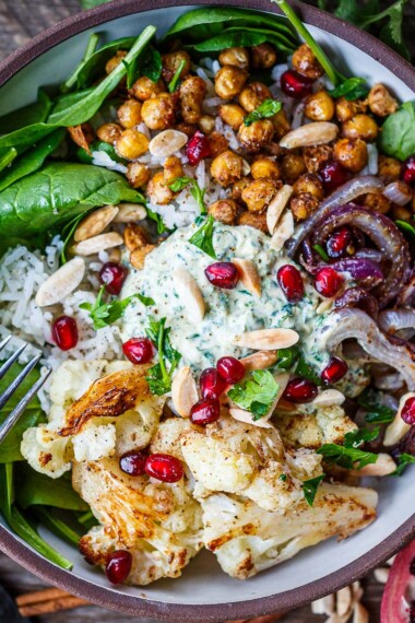 You'll love these roasted Cauliflower Chickpea Bowls! Spiced cauliflower and chickpeas served over Moroccan rice with spinach, almonds, and pomegranate seeds. A tasty wholesome dinner bursting with flavor! Vegan-adaptable.