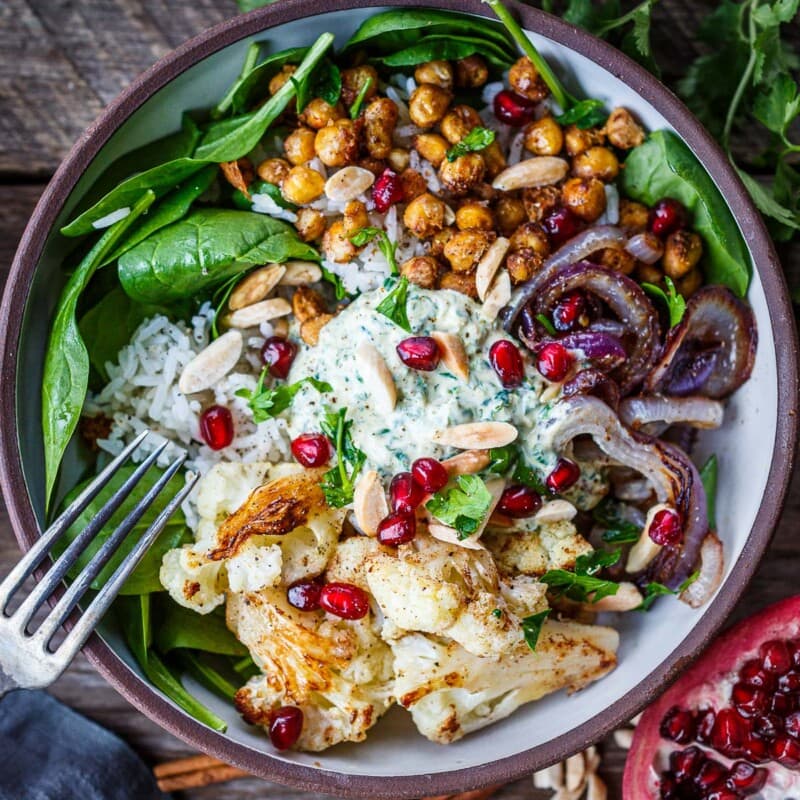 You'll love these roasted Cauliflower Chickpea Bowls! Spiced cauliflower and chickpeas served over Moroccan rice with spinach, almonds, and pomegranate seeds. A tasty wholesome dinner bursting with flavor! Vegan-adaptable.