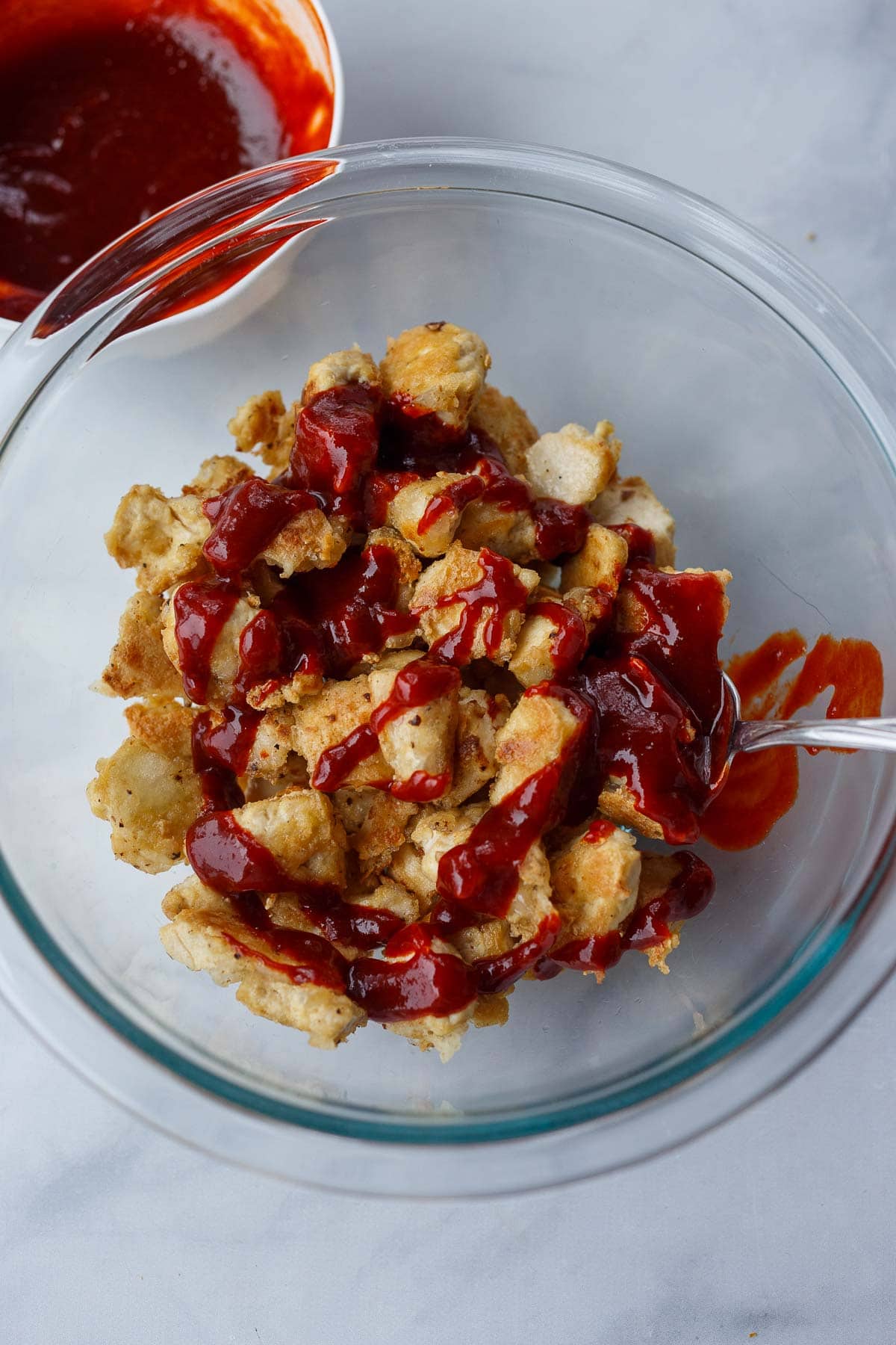 glass mixing bowl with fried tofu pieces and gochujang sauce poured over top.