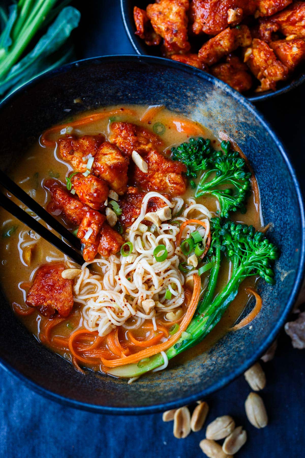 bowl of peanut butter ramen with noodles, topped with crispy Korean tofu, broccolini, carrots, peanuts, green onions.