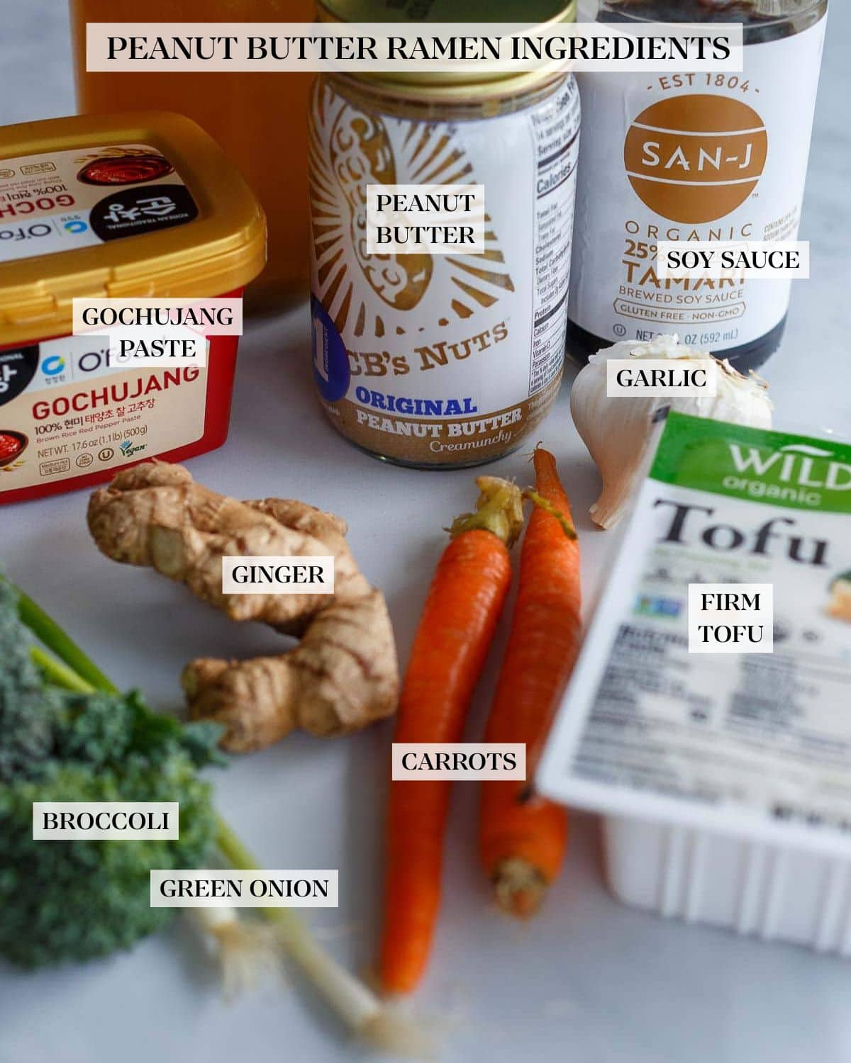 ingredients laid out for peanut butter ramen - tofu, tamari, garlic, peanut butter, homemade veggie broth, gochujang, ginger, carrots, broccoli, scallions.