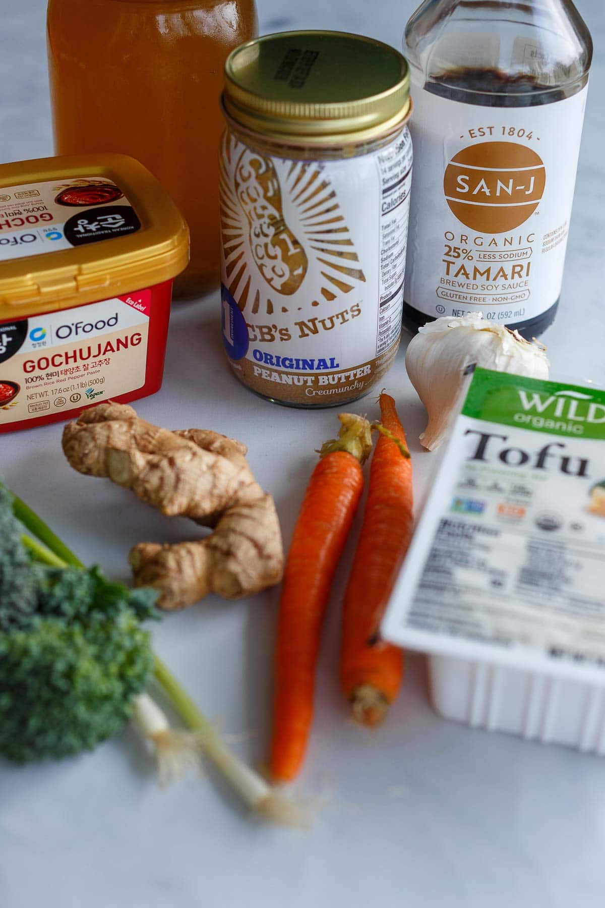 ingredients laid out for peanut butter ramen - tofu, tamari, garlic, peanut butter, homemade veggie broth, gochujang, ginger, carrots, broccoli, scallions.