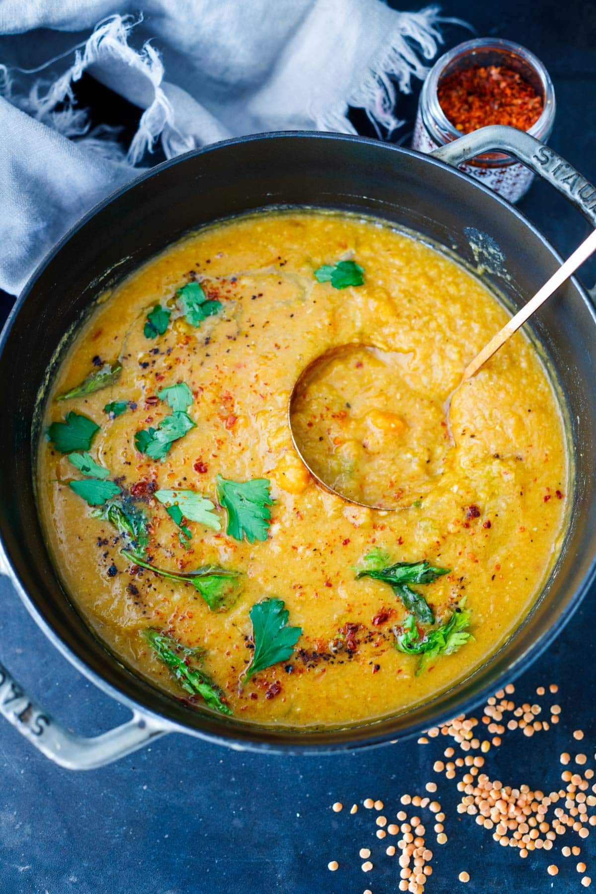 creamy red lentil soup in pot with ladle, garnished with parsley, aleppo chili flakes, sumac.