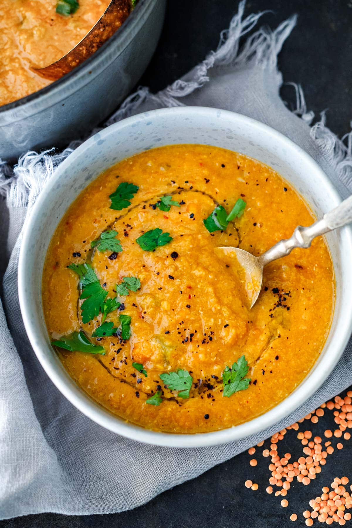 red lentil soup in a bowl with drizzle of olive oil, parsley, sumac.