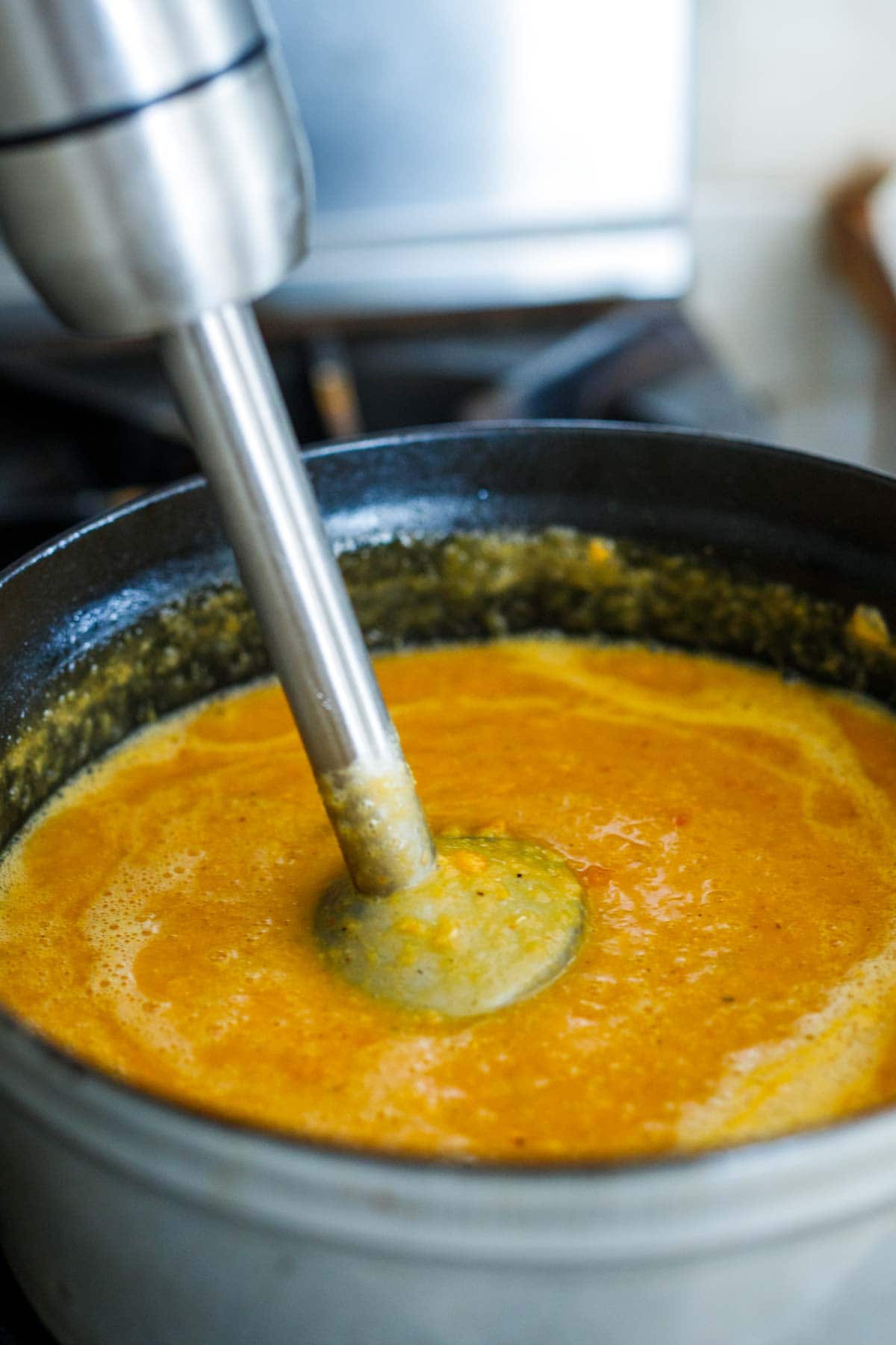 immersion blender pureeing red lentil soup to create creamy texture.