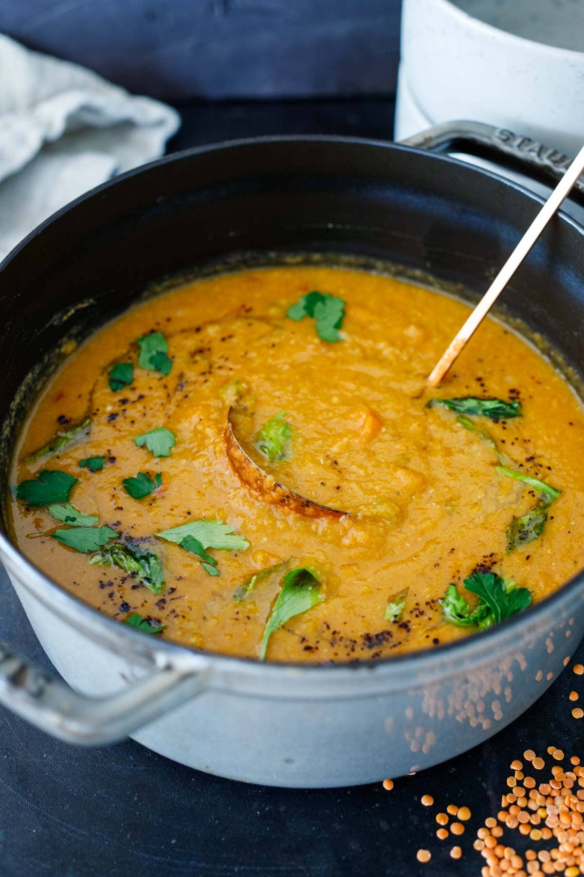 creamy red lentil soup in dutch oven garnished with parsley and sumac.