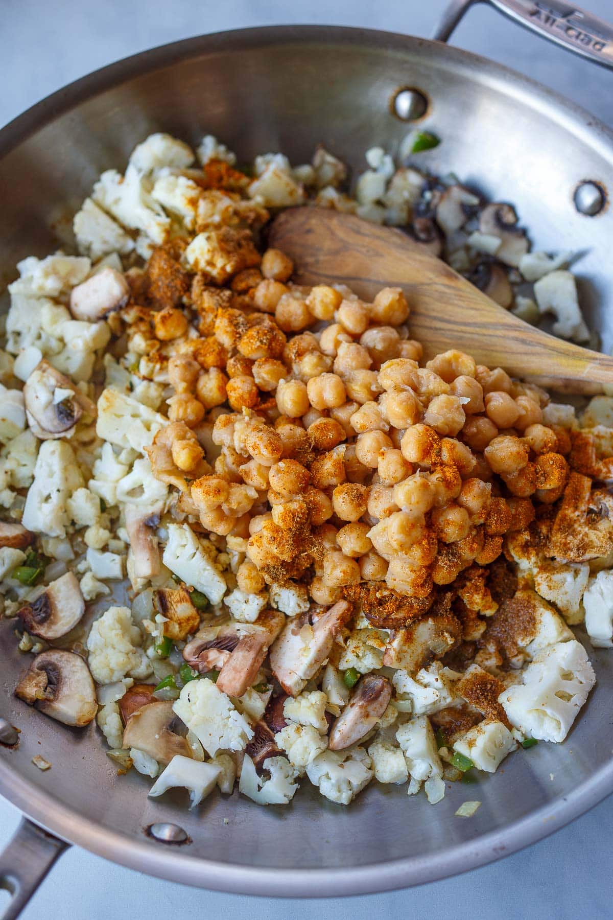 chickpeas and spices added to frying pan with mushrooms, cauliflower, onions.