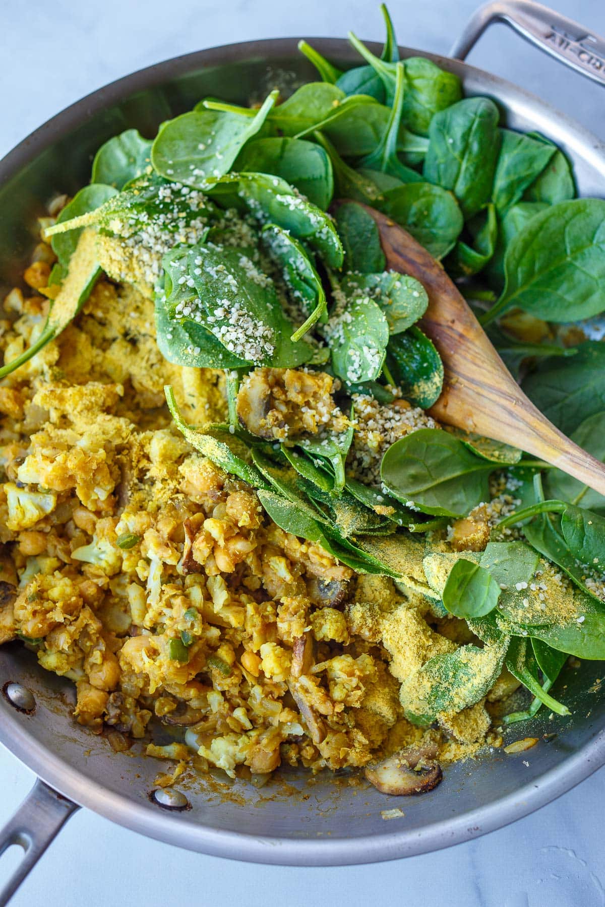 chickpea scramble with fresh spinach, hemp seeds, nutritional yeast added to pan.