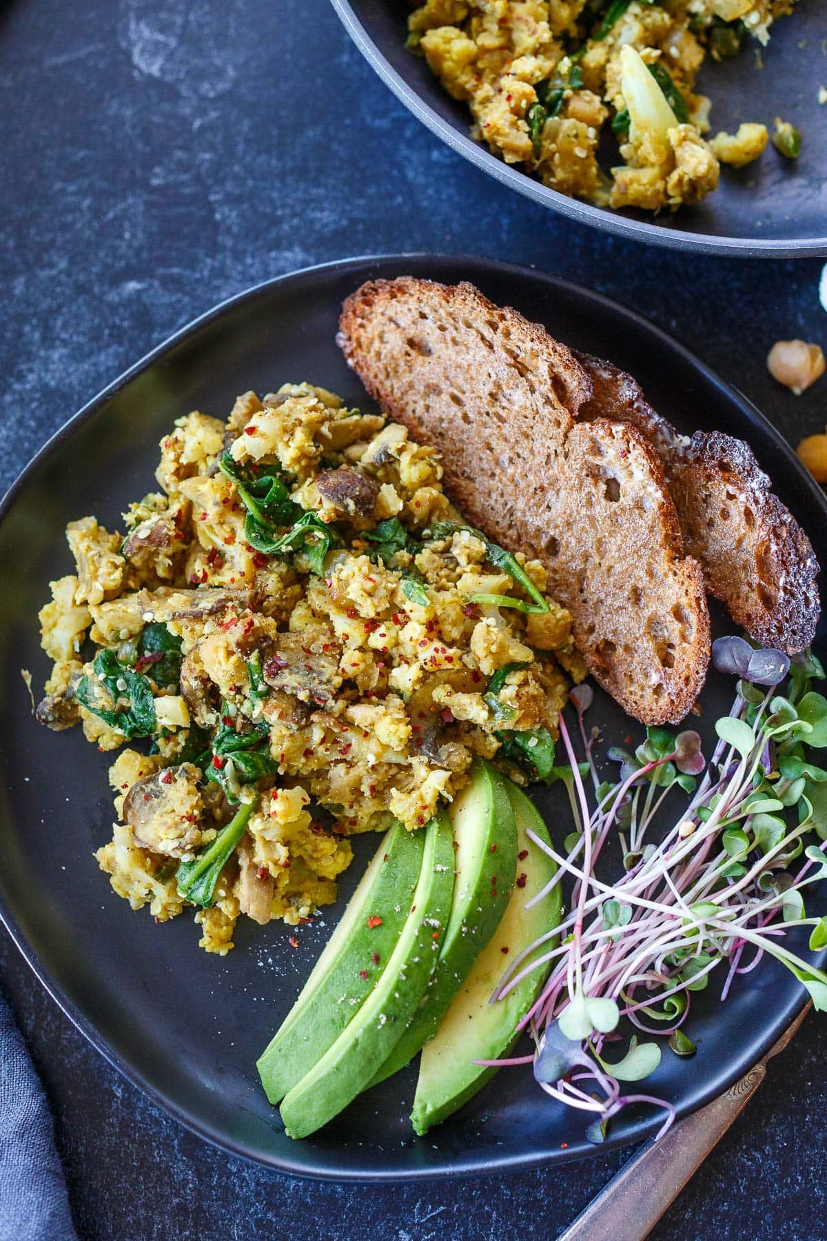 breakfast plate with chickpea scramble, toast, avocado slices, and microgreens.
