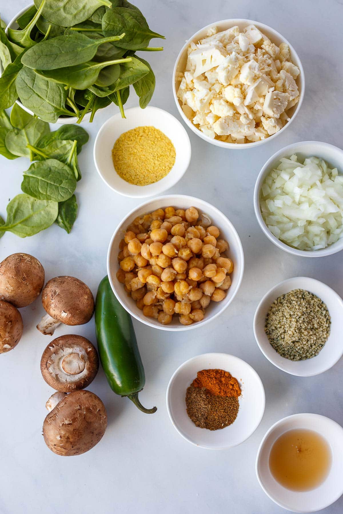 ingredients for chickpea scramble in bowls - chickpeas, onions, cauliflower, nutritional yeast, spices, hemp seeds, oil, spinach, mushrooms, jalapeno.