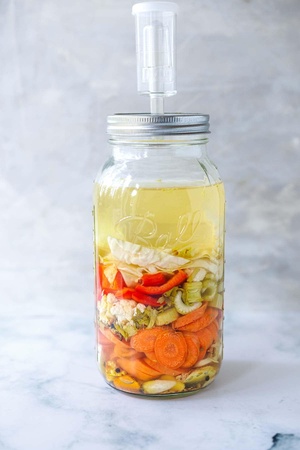 fermented gut shot in mason jar with vegetables and liquid sealed with an airlock.