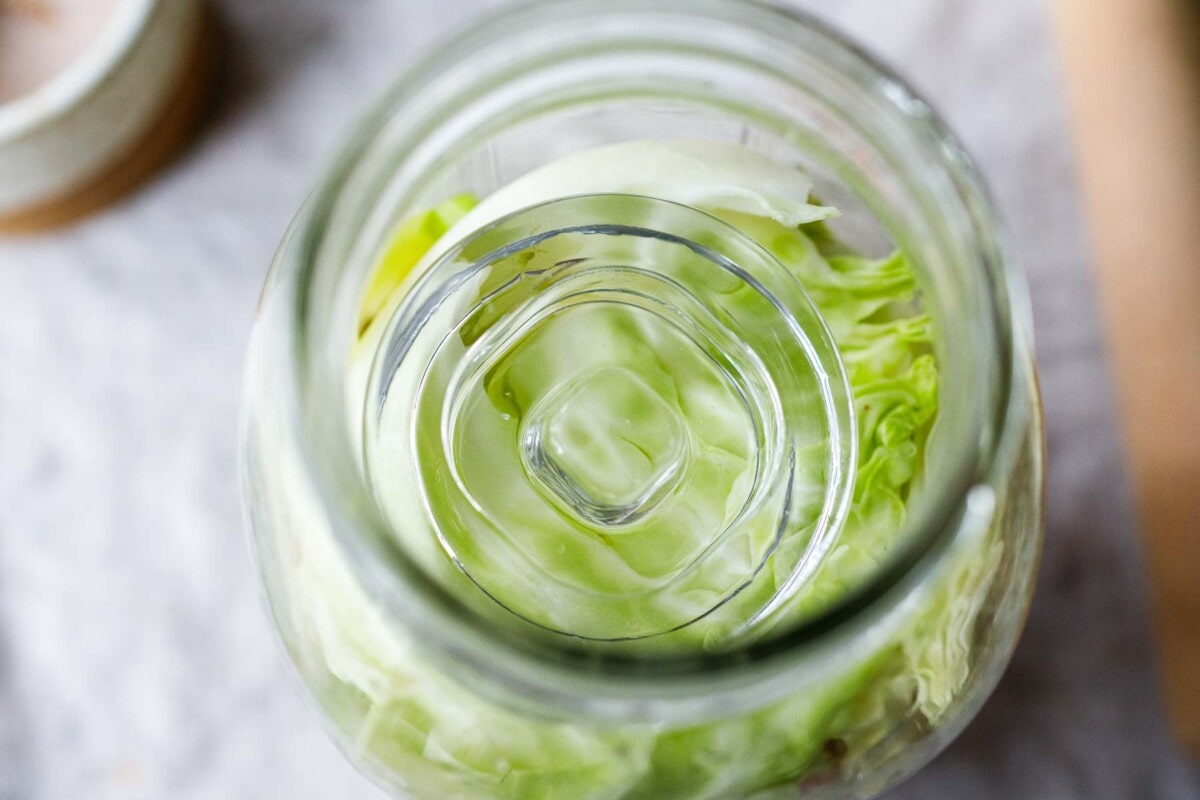 fermentation weight on top of cabbage leaves in glass jar.