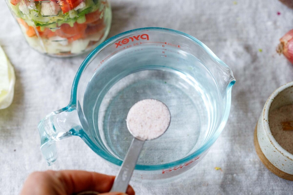 filtered water in measuring cup with teaspoon of salt over top to make a brine for the gut shot.