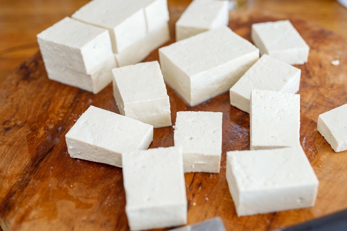 tofu cut into cubes on wood cutting board.