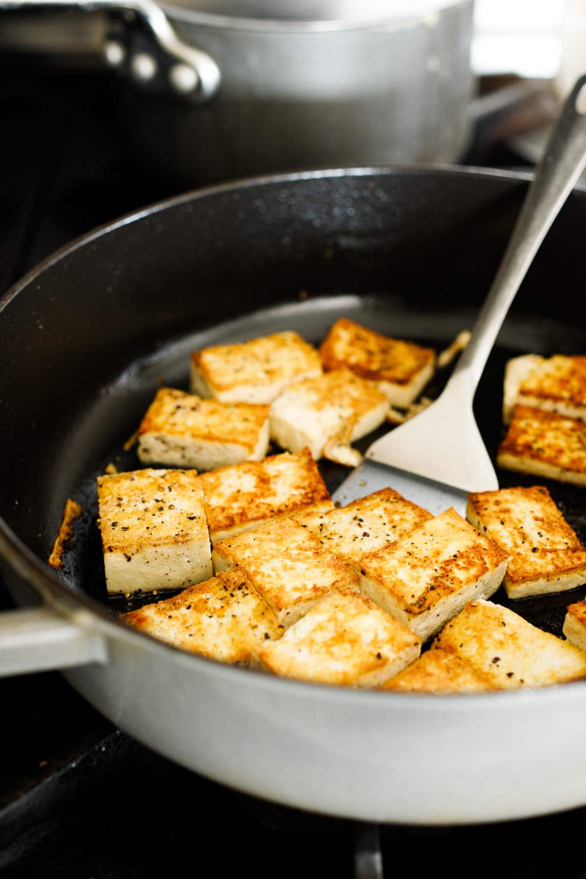 cubed tofu frying in pan, seasoned with salt and pepper.