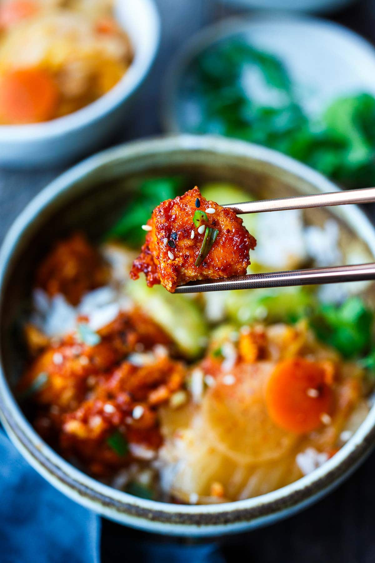 chopsticks holding korean tofu over korean tofu rice bowl