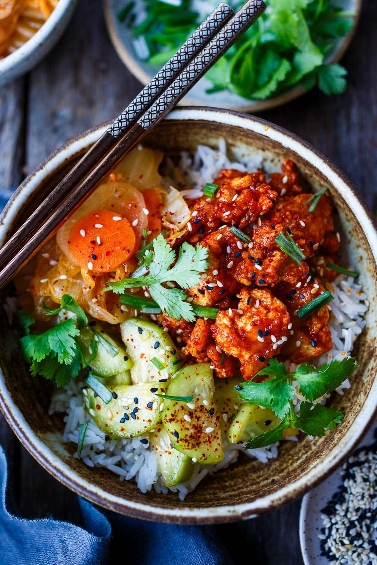 crispy korean tofu rice bowl on steamed jasmine rice served with kimchi and cucumber salad.