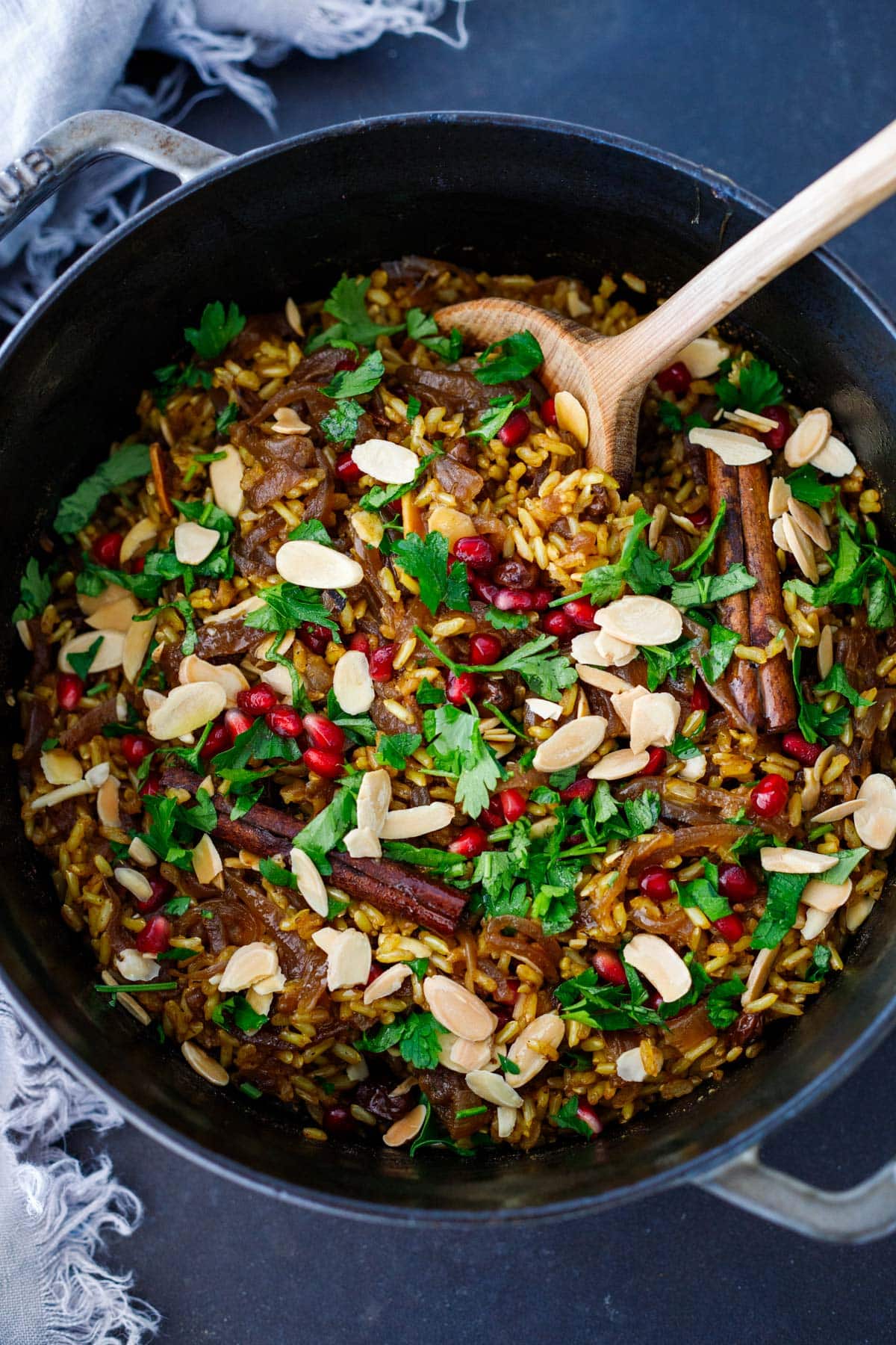 cooked Moroccan rice pilaf with cinnamon sticks in Dutch oven, garnished with minced parsley, pomegranate seeds, and slivered almonds.