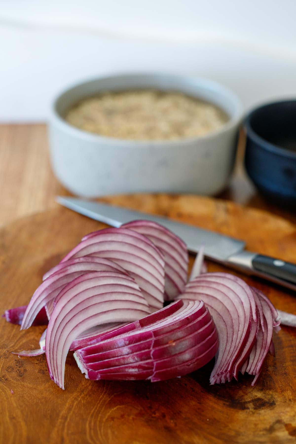 thinly sliced red onion on wood cutting board.