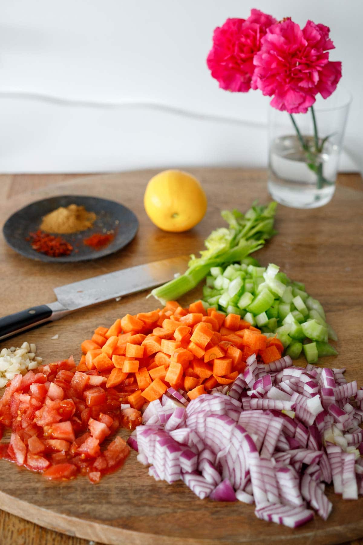 diced red onion, tomato, garlic, carrots, celery on wood board.