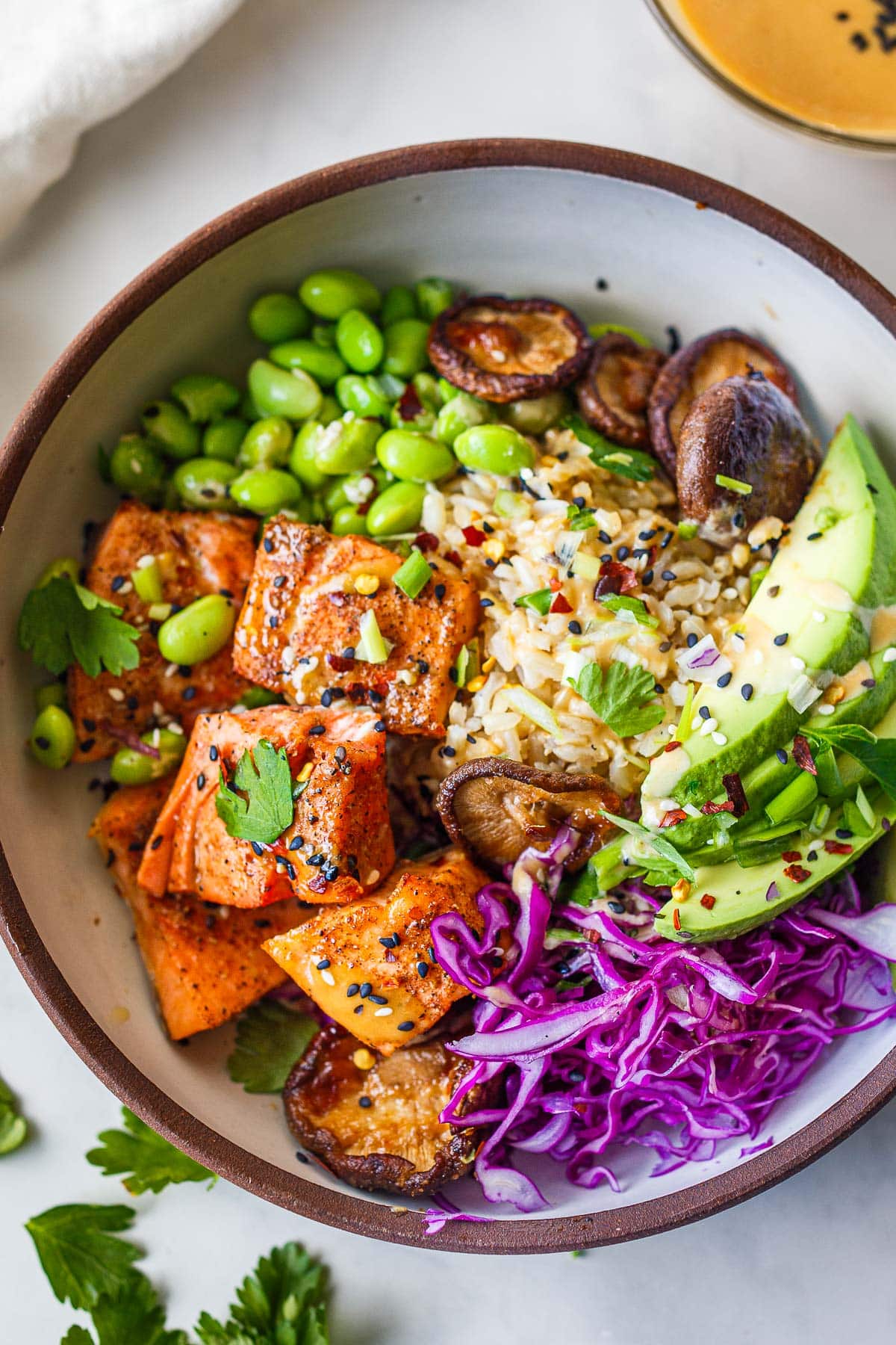 This Salmon Bowl is brimming with healthy protein, healthy veggies, and savory Asian flavors. Salmon bites are paired with roasted shiitake mushrooms, edamame, avocado, and red cabbage drizzled with a delicious miso dressing.