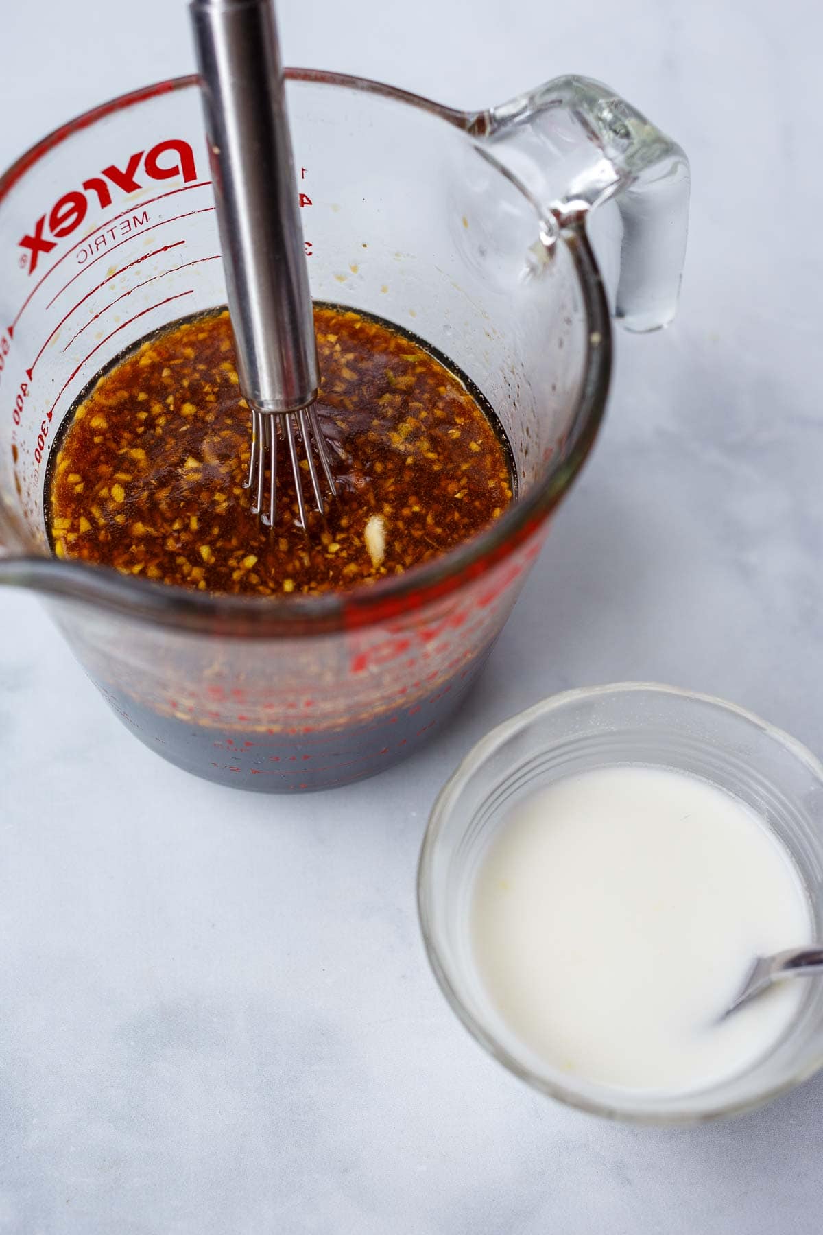 teriyaki sauce in glass measuring cup with whisk next to cornstarch mixture.