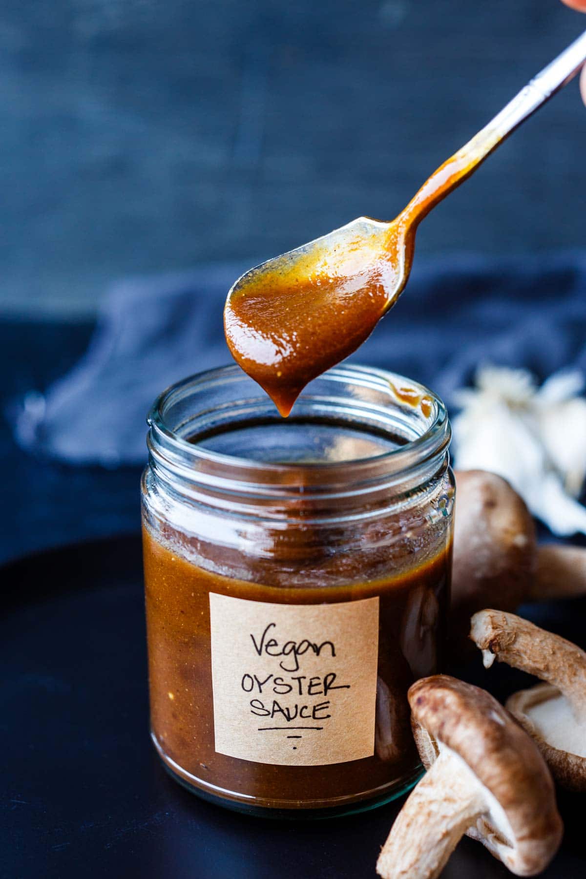 jar of homemade vegan oyster sauce with spoonful of sauce held over top.