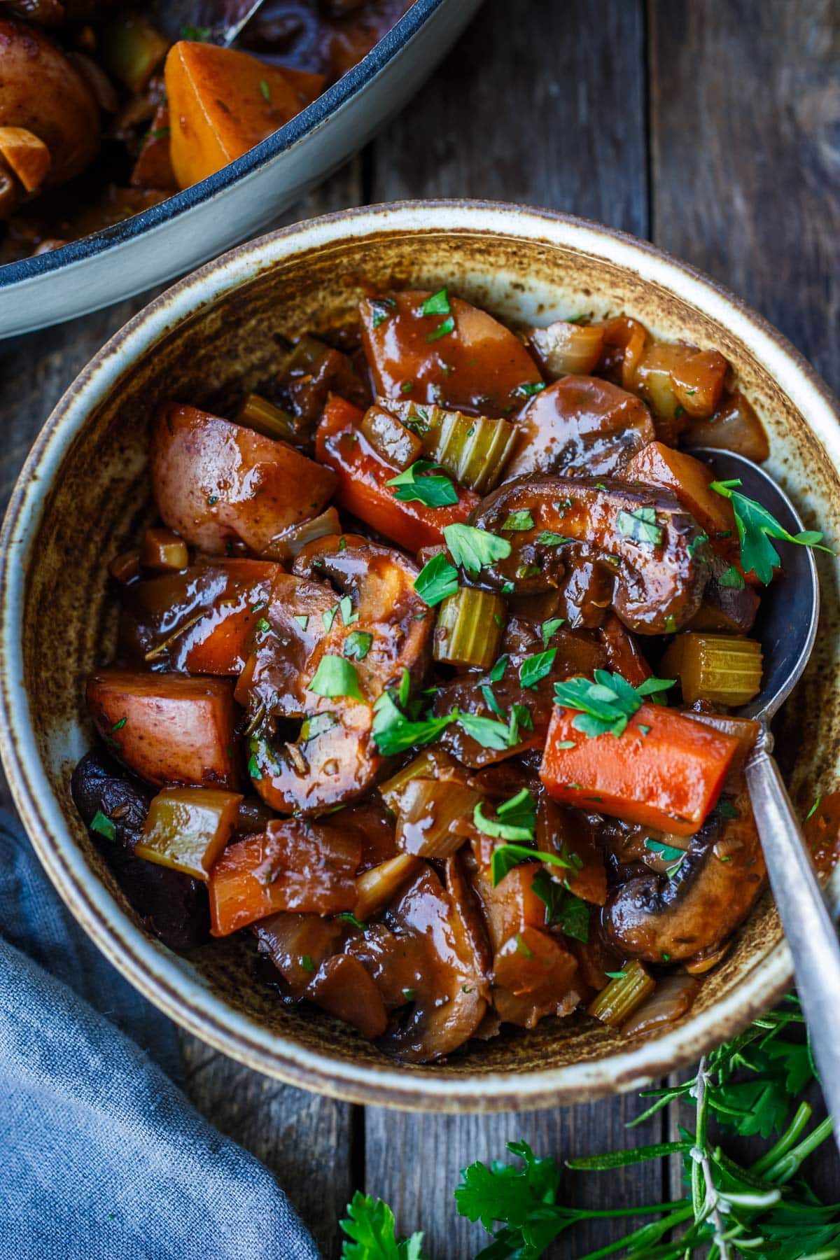 vegan vegetable stew in bowl with tender veggies- mushrooms, carrots, celery, garnished with parsley.