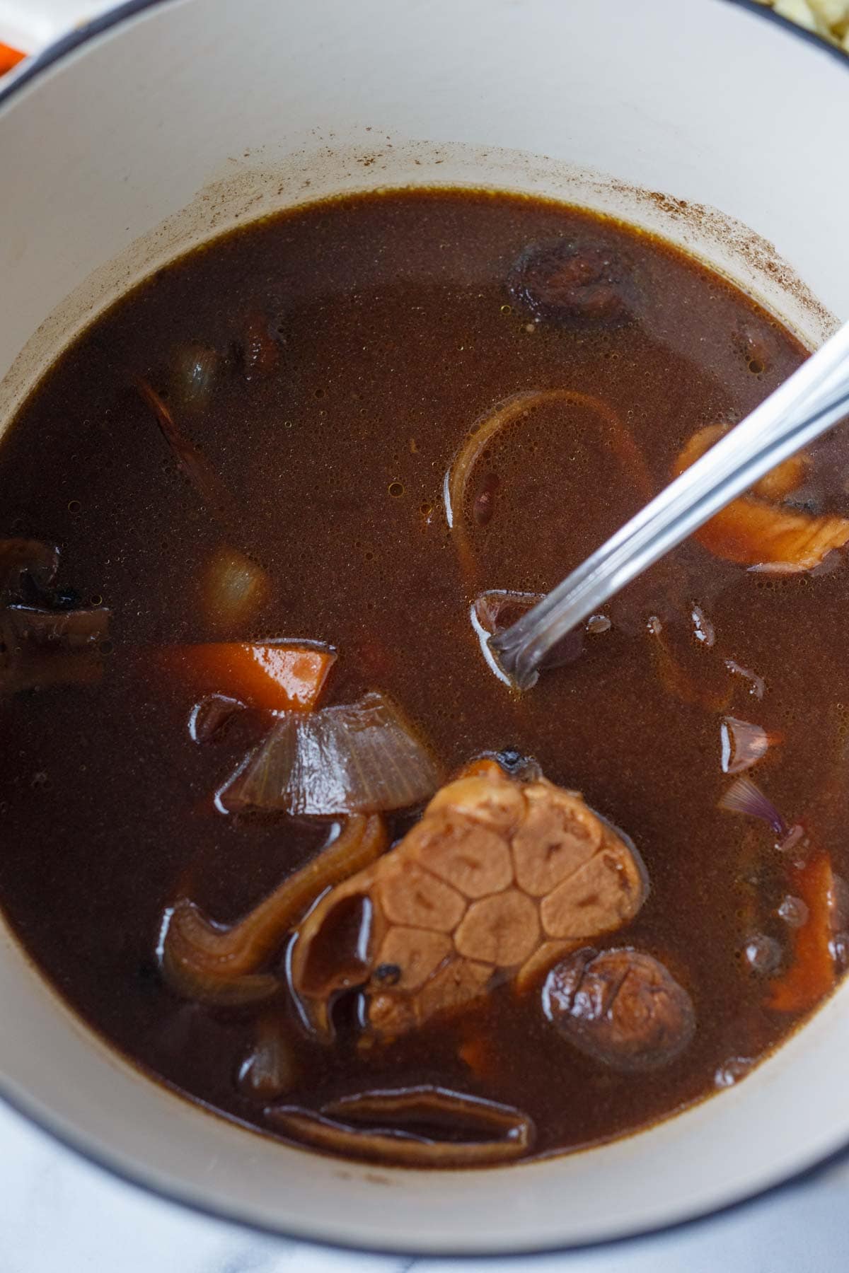 homemade vegetable broth stewing- garlic head, shallots, carrots in dark broth.