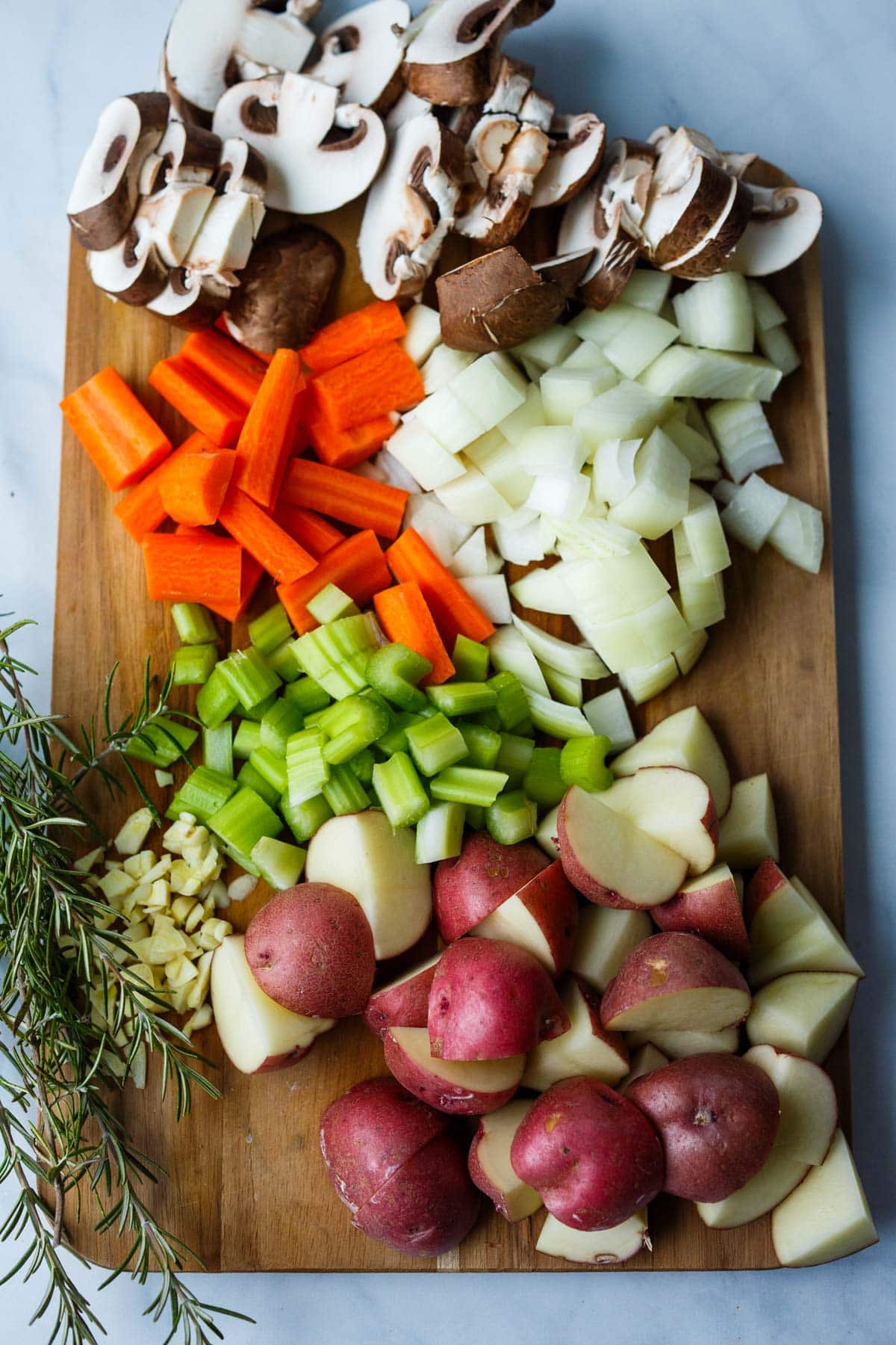 chopped veggies for vegetable stew on wood cutting board with fresh thyme - mushrooms, onion, carrots, celery, garlic, potatoes. 