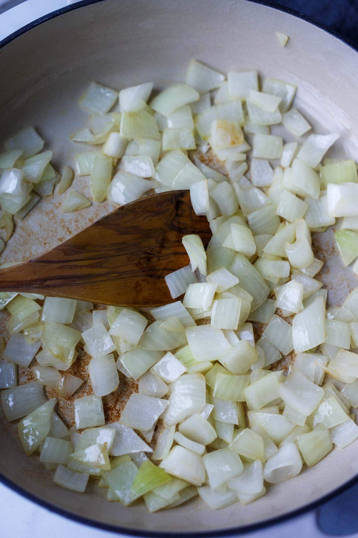 chopped onions sautéing in pan, stirred with wood spoon.