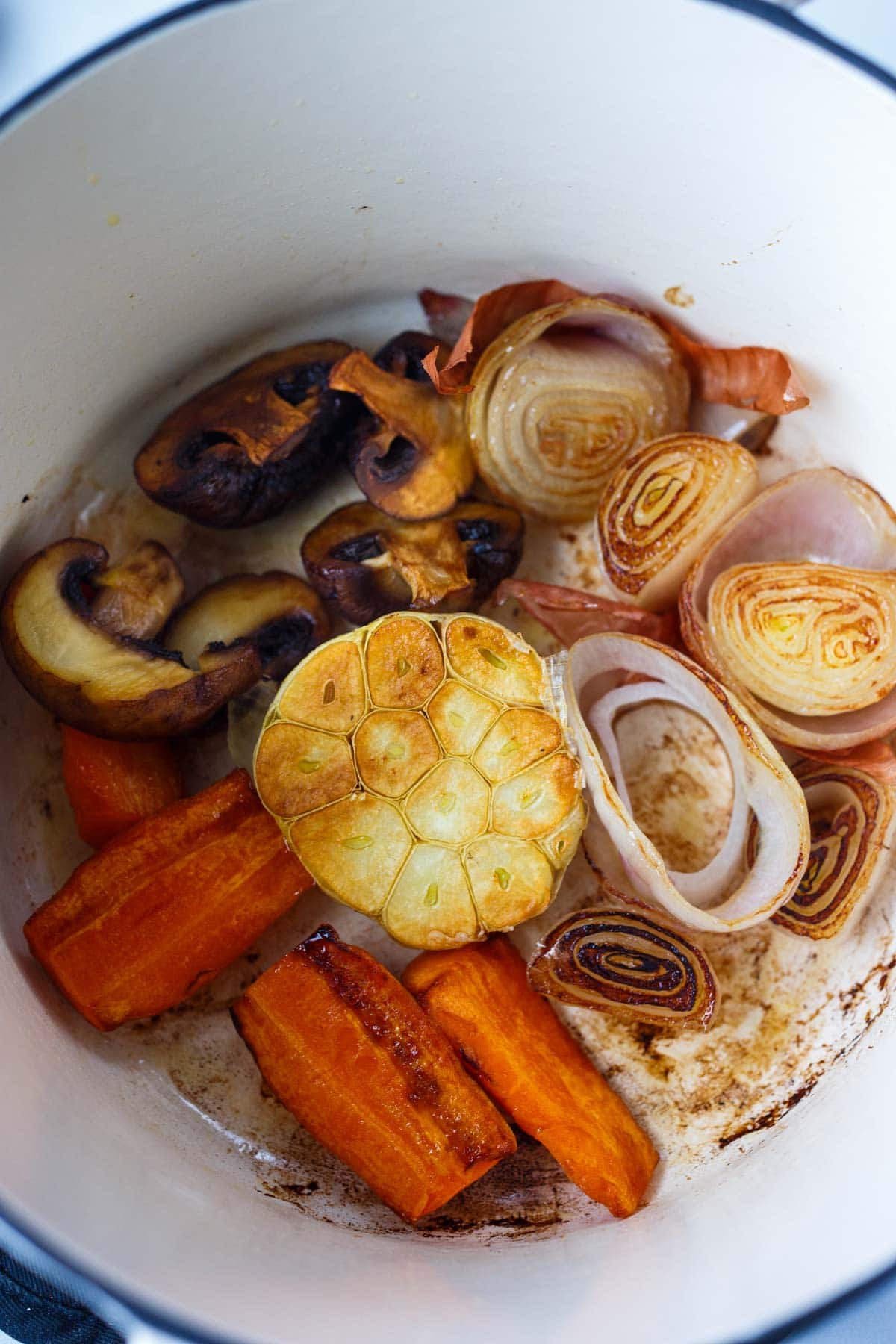 dutch oven with garlic head, shallots, carrots, mushrooms to make vegetable broth for stew.