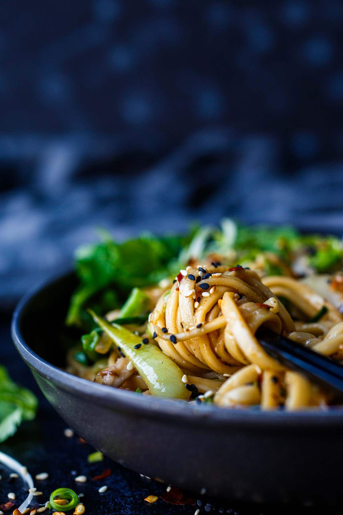chopsticks holding twirl of longevity noodles over bowl, garnished with sesame seeds.
