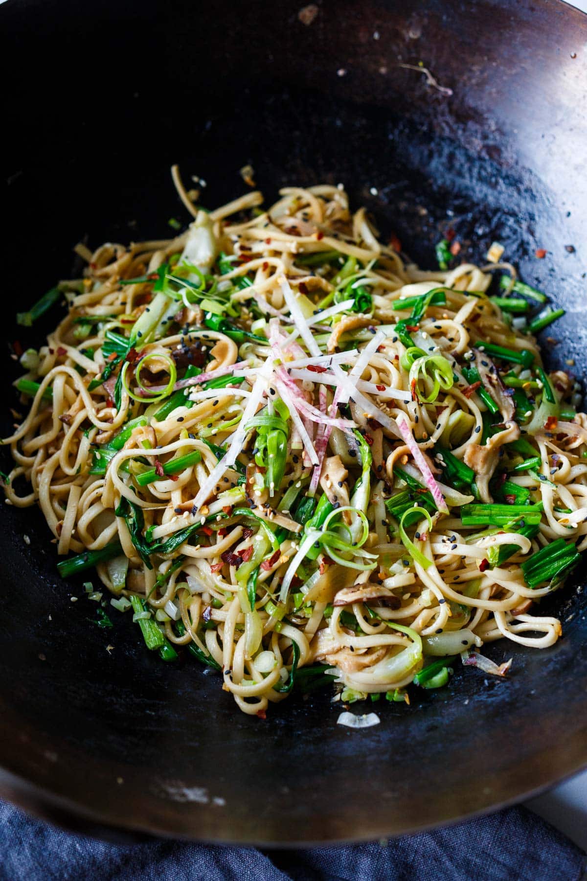 large wok with longevity noodles, garnished with scallions, chili flakes, watermelon radish.