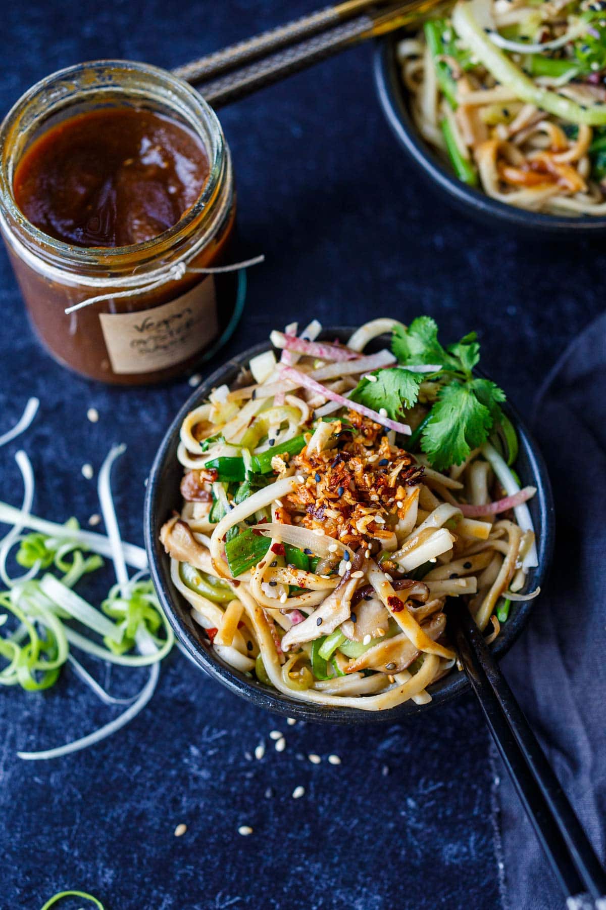 bowl of longevity noodles with chili crisp, next to jar of homemade vegan oyster sauce.