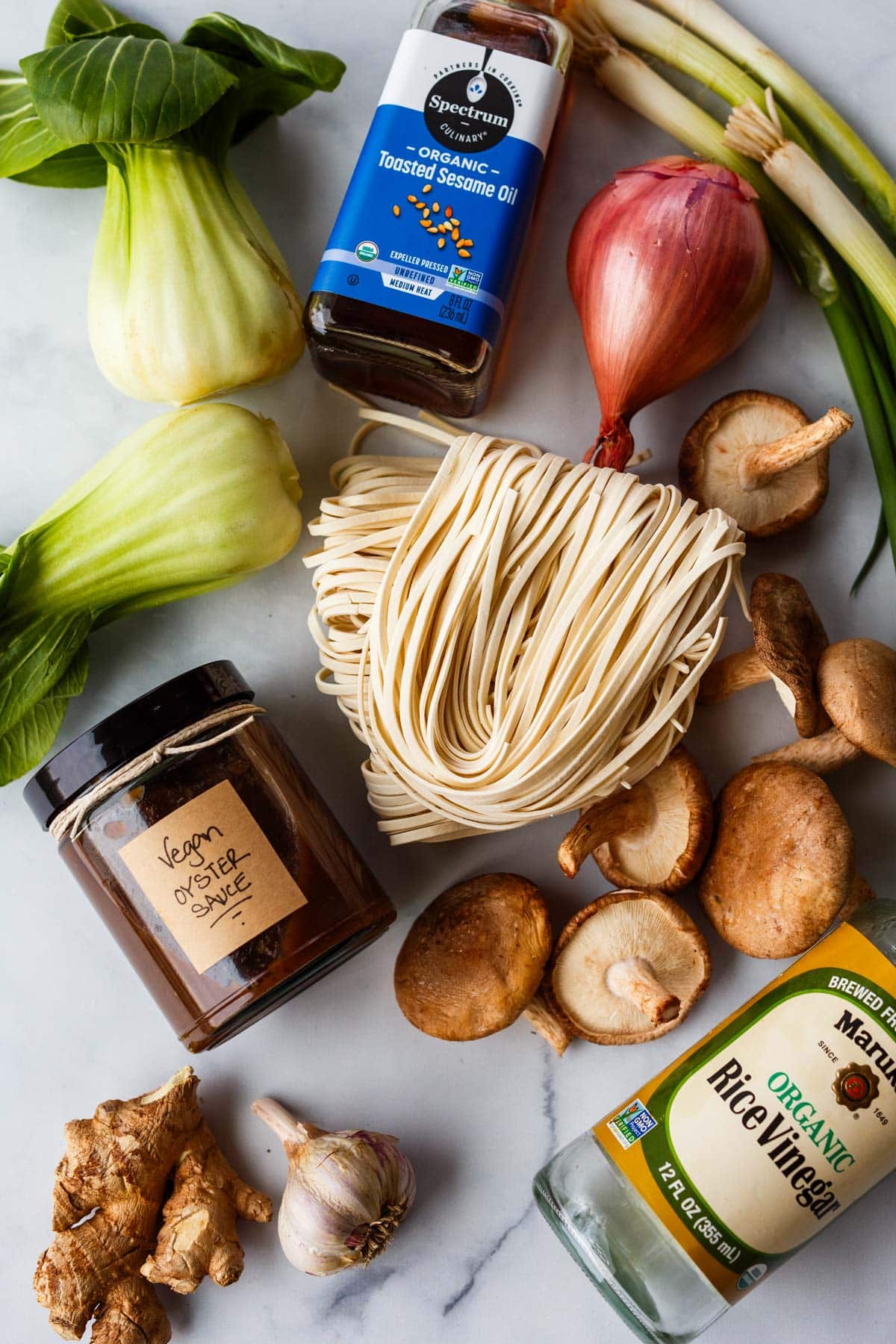 ingredients to make longevity noodles - jar of homemade vegan oyster sauce, bok choy, toasted sesame oil, shallot, scallions, shiitake mushrooms, long noodles, rice vinegar, ginger.