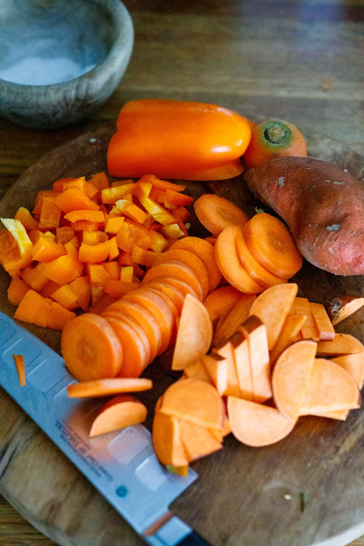 orange veggies for vegan queso recipe sliced thin on wood cutting board with sharp knife.